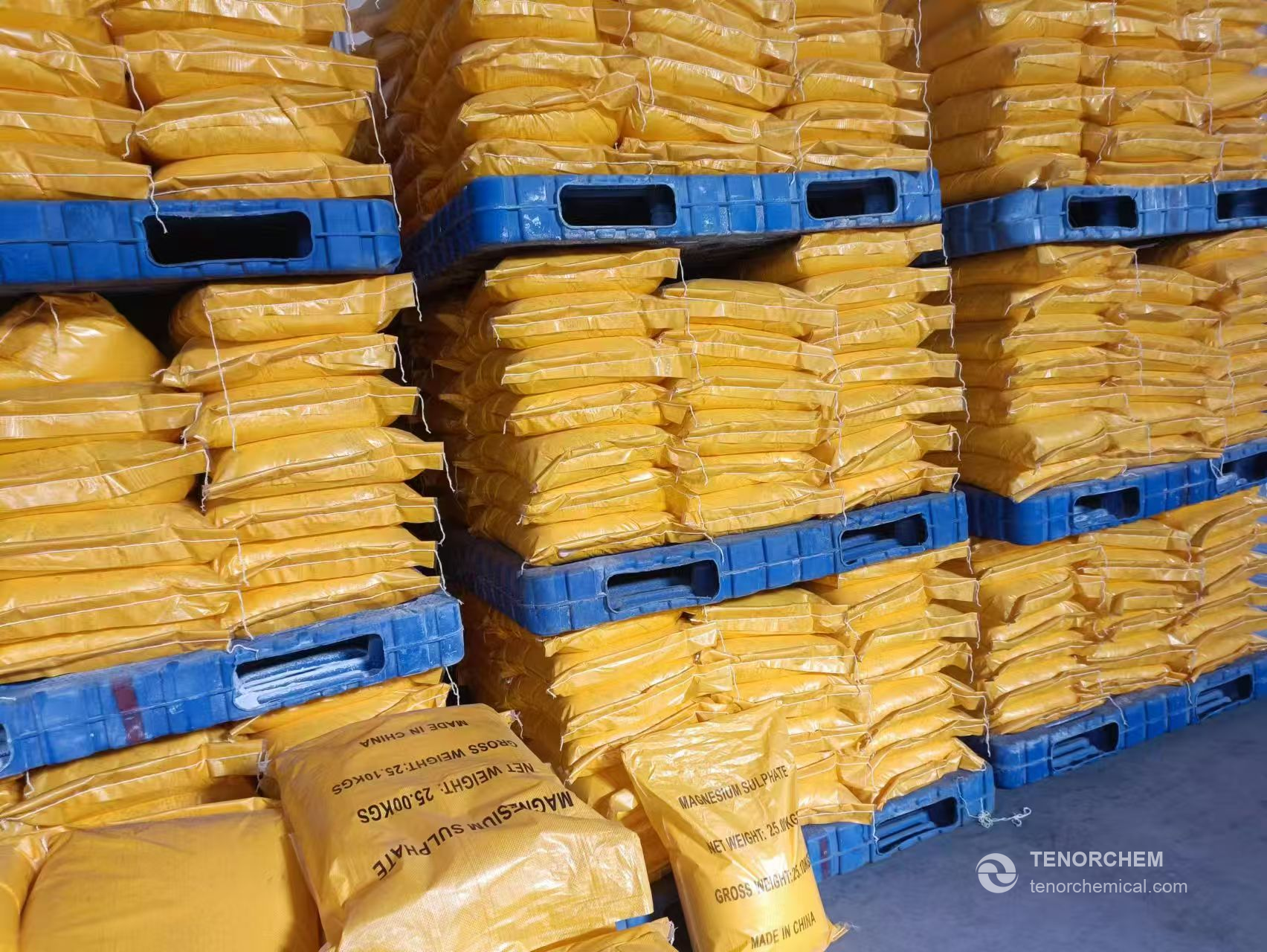 Stacks of yellow magnesium sulfate bags on blue pallets in a warehouse